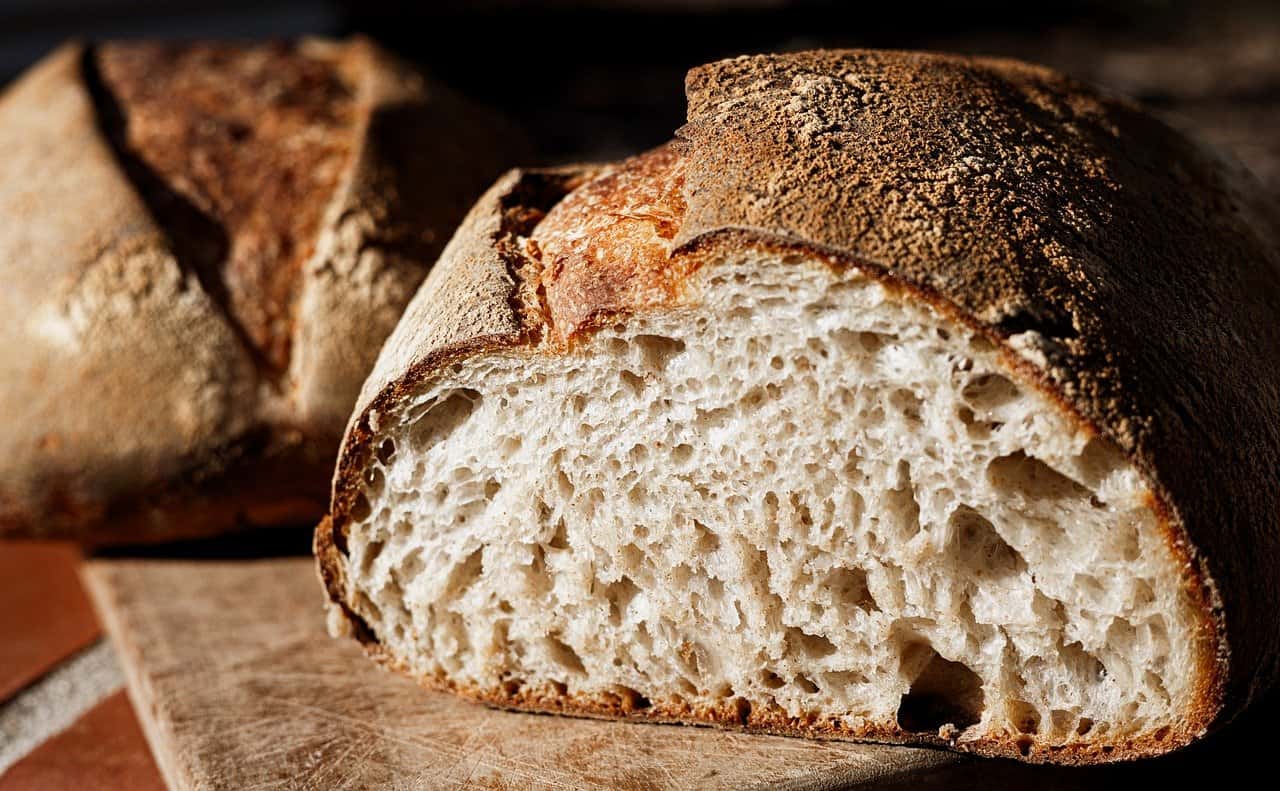 Close-up of sliced artisanal bread with a crunchy crust and airy crumb, resting on a wooden cutting board under natural light.